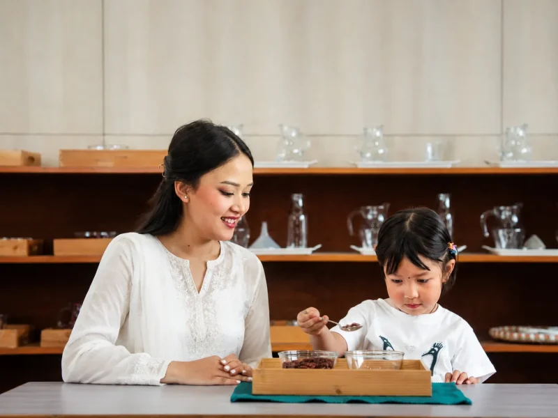 Teacher smiling as a child works on a tray at the table